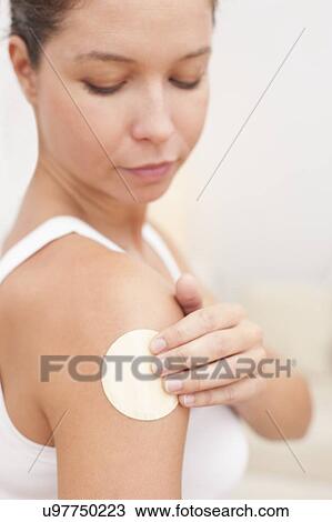 Stock Image - Woman applying nicotine path to arm. Fotosearch