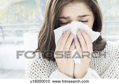 Stock Image - Woman blowing nose on tissue. Fotosearch