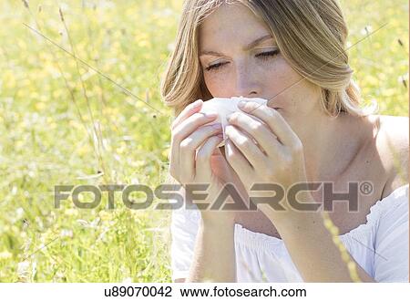 Stock Image - Woman blowing nose on tissue. Fotosearch