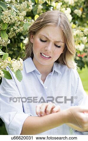 Stock Image - Woman by tree scratching arm. Fotosearch