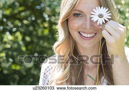 Stock Image - Woman holding daisy in front of eye. Fotosearch