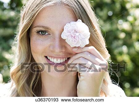 Stock Image - Woman holding flower in front of eye. Fotosearch