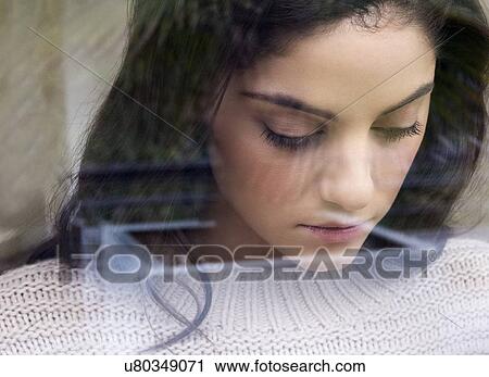 Stock Image - Woman looking down, view through reflective glass. Fotosearch