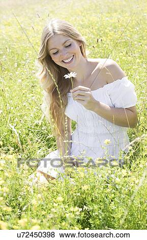 Woman sitting in meadow holding daisy View Large Photo Image Stock Photo - Woman sitting in meadow holding daisy. Fotosearch