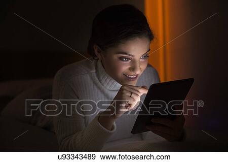 Woman using digital tablet in dark room View Large Photo Image Stock Photo - Woman using digital tablet in dark room. Fotosearch