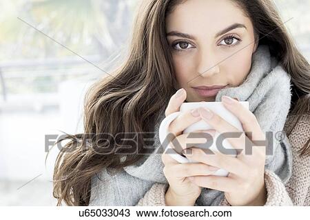 Stock Image - Woman wearing grey scarf holding mug. Fotosearch