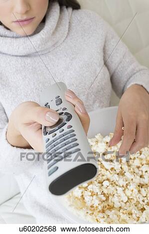 Stock Photo - Woman with tv remote eating popcorn. Fotosearch