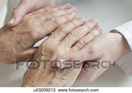 Stock Image - Female doctor examining senior patient's hands. Fotosearch