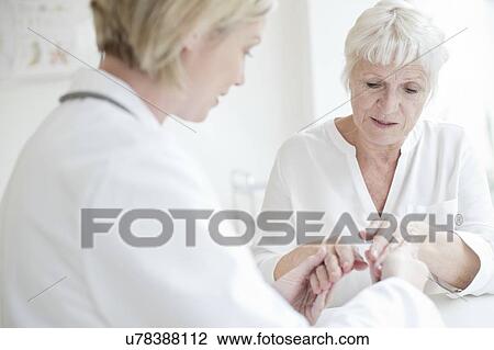 Stock Image - Female doctor examining senior patient's hand. Fotosearch