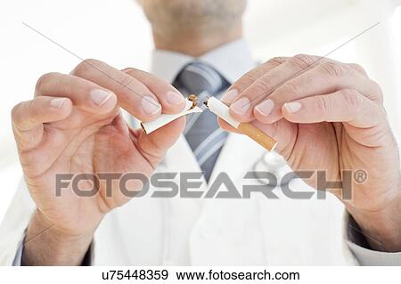 Male doctor breaking cigarette in two View Large Photo Image Stock Photo - Male doctor breaking cigarette in two. Fotosearch