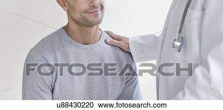 Stock Image - Male doctor with hand on patient's shoulder. Fotosearch