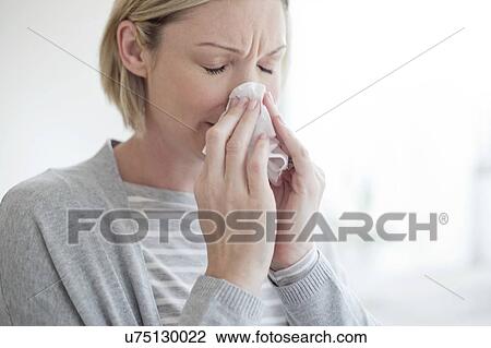 Stock Image - Mid adult woman blowing her nose. Fotosearch