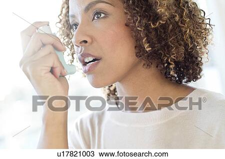 Stock Image - Mid adult woman using inhaler. Fotosearch