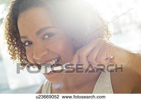 Stock Image - Portrait of woman brushing teeth. Fotosearch