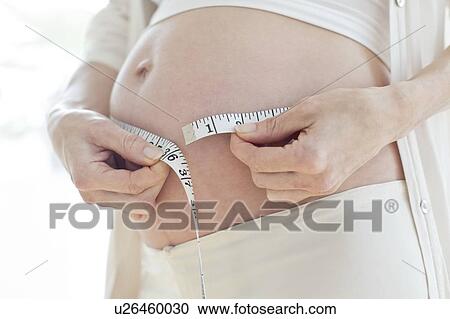 Stock Image - Pregnant woman measuring tummy. Fotosearch