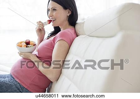 Pregnant woman on sofa eating fresh fruit View Large Photo Image Stock Image - Pregnant woman on sofa eating fresh fruit. Fotosearch