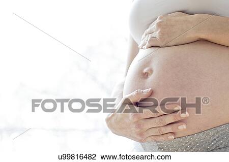 Stock Image - Pregnant woman touching tummy. Fotosearch