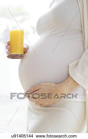 Picture - Pregnant woman touching tummy with juice. Fotosearch