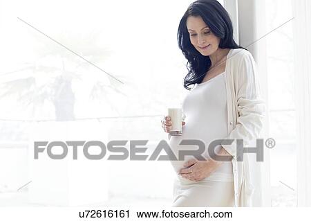 Stock Image - Pregnant woman touching tummy with milk. Fotosearch