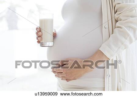 Stock Photo - Pregnant woman touching tummy with milk. Fotosearch