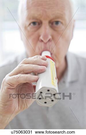 Stock Image - Senior man using peak flow metre. Fotosearch