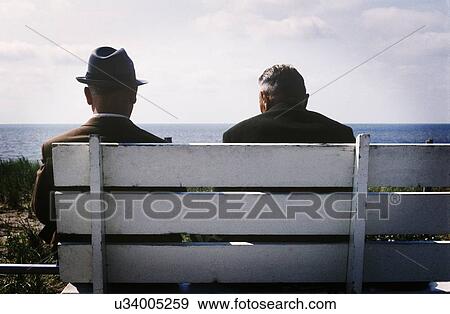 Stock Photo - Two men sitting on bench by sea. Fotosearch