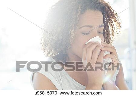 Stock Image - Woman blowing nose on tissue. Fotosearch