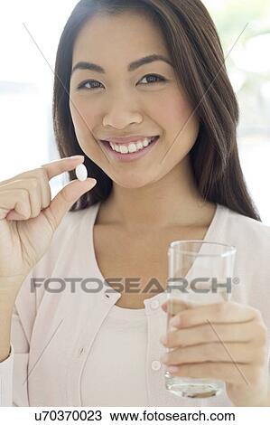 Stock Image - Woman holding pill and glass of water. Fotosearch