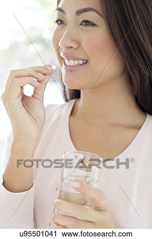 Stock Image - Woman holding pill and glass of water. Fotosearch