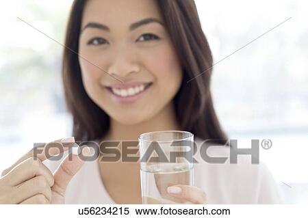 Stock Photography - Woman holding pill and glass of water. Fotosearch