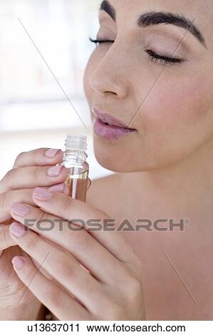 Stock Image - Woman smelling liquid in small glass bottle. Fotosearch