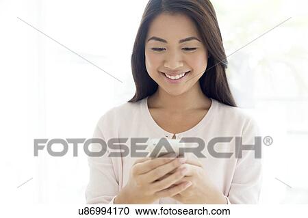 Stock Image - Woman using smartphone, smiling. Fotosearch