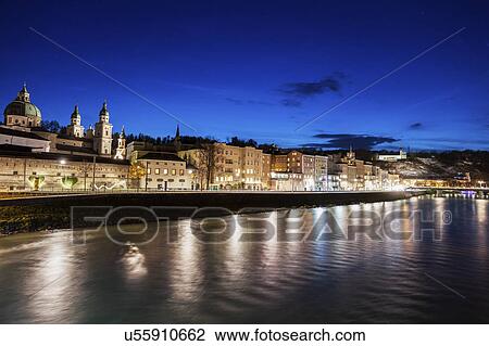 Stock Image - Austria, Salzburg, Riverbank with buildings at night. Fotosearch
