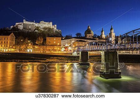 Stock Photo - Austria, Salzburg, Riverbank with buildings at night. Fotosearch