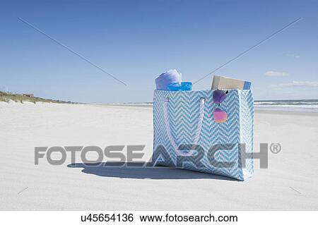 Stock Photograph - Bag with towel, book and sunglasses on empty beach. Fotosearch