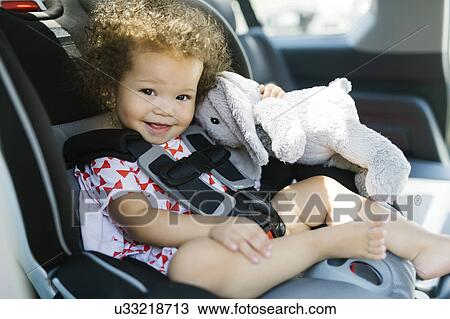 Stock Image - Girl (12-17) sitting on car seat and holding plush toy. Fotosearch