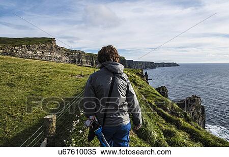 Stock Photography - Ireland, County Clare, Woman walking along Cliffs of Moher. Fotosearch