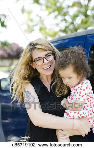 Mother carrying daughter (12-17 months) in front of car View Large Photo Image Stock Image - Mother carrying daughter (12-17 months) in front of car. Fotosearch