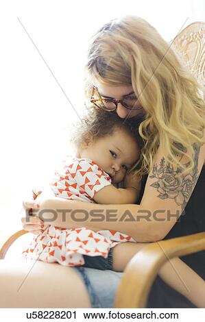 Stock Image - Mother sitting on chair and embracing daughter (12-17 months). Fotosearch