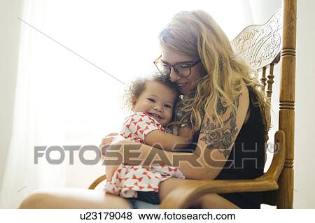 Stock Photo - Mother sitting on chair and rocking daughter (12-17 months). Fotosearch