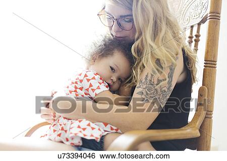 Stock Photograph - Mother sitting on chair and rocking daughter (12-17 months). Fotosearch