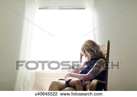 Stock Image - Mother sitting on chair and breastfeeding daughter (12-17 months). Fotosearch