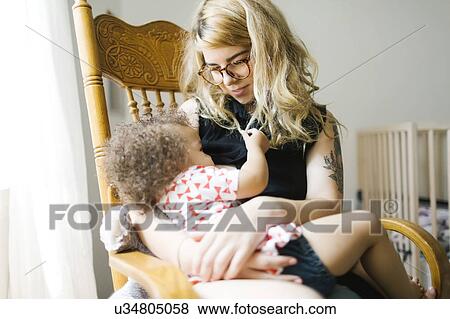 Stock Photo - Mother sitting on chair and breastfeeding daughter (12-17 months). Fotosearch