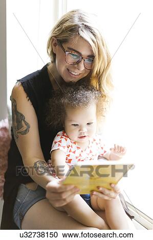 Mother sitting with daughter (12-17 months) on windowsill and reading book View Large Photo Image Stock Image - Mother sitting with daughter (12-17 months) on windowsill and reading book. Fotosearch