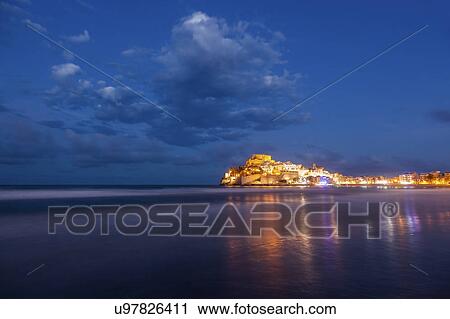 Stock Image - Spain, Valencian Community, Peniscola, Illuminated town by sea. Fotosearch