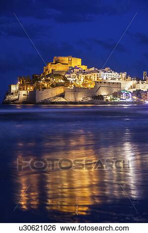 Stock Photograph - Spain, Valencian Community, Peniscola, Town with fortified wall by sea at dusk. Fotosearch
