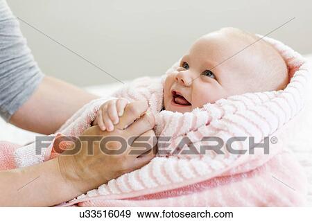 Stock Photo - Baby boy (12-17 months) in pink blanket holding mom's hand and smiling. Fotosearch