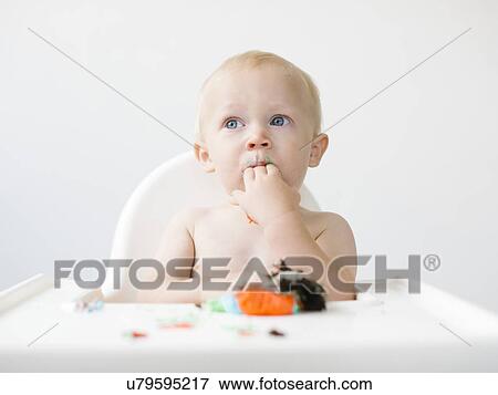 Stock Photo - Baby boy (12-17 months) sitting in high chair and eating cupcake. Fotosearch