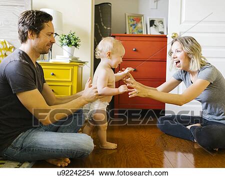 Picture - Baby boy (12-17 months) taking first steps with parents at home. Fotosearch