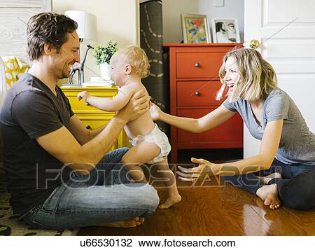Stock Image - Baby boy (12-17 months) taking first steps with parents at home. Fotosearch